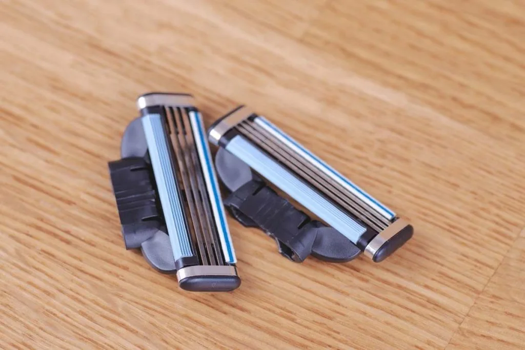 Two cartridge razor heads resting on a wooden surface, showing the lubricating strips.
